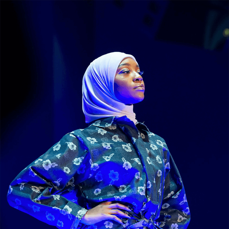 A model at the 2018 Howard University Homecoming Fashion Show. She wears a hijab and an outfit printed with tropical flowers.