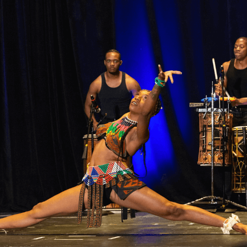A dancer from the group Step Afrika! accompanied by two drummers.