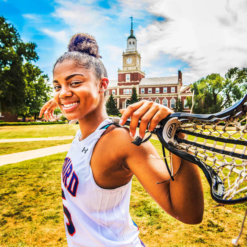 A Howard University athlete holding a lacrosse stick over her shoulders.