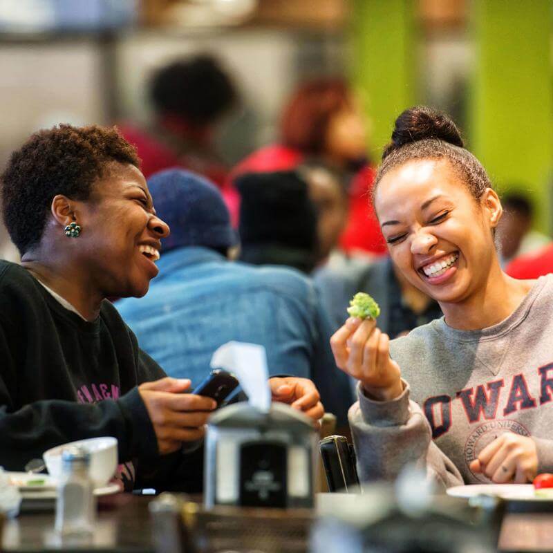 Two laughing women in a dining hall setting.