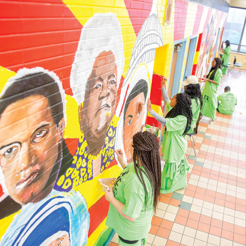 Howard students on Alternative Spring Break painting a mural inside a building.