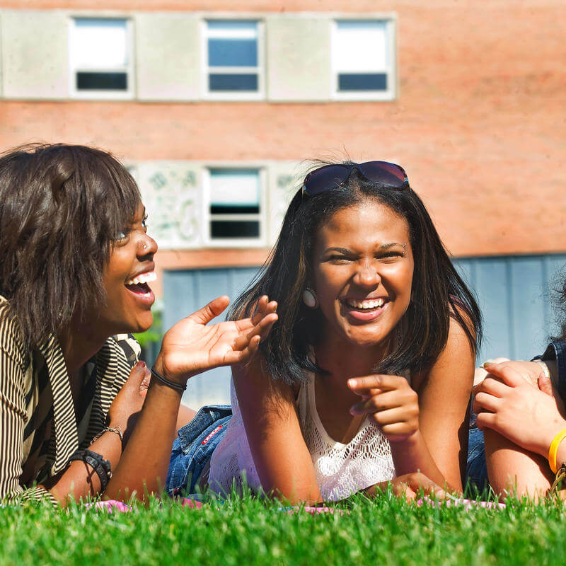 Three students conversing as they lay on the grass in front of a Howard University building.