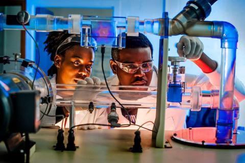 Two students in protective gear conducting chemistry research.