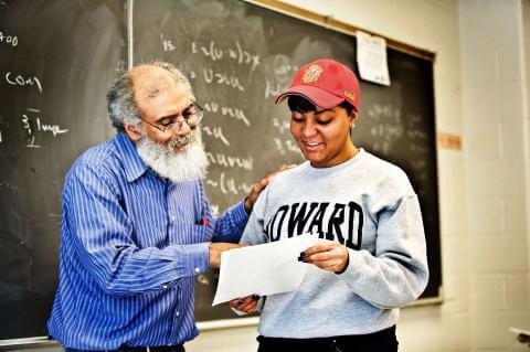 A student in a Howard brand shirt receiving instruction on a paper from a professor in a classroom setting.