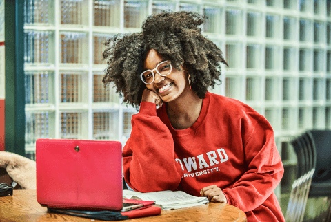 A student in a Howard sweatshirt with a laptop and notes on paper.