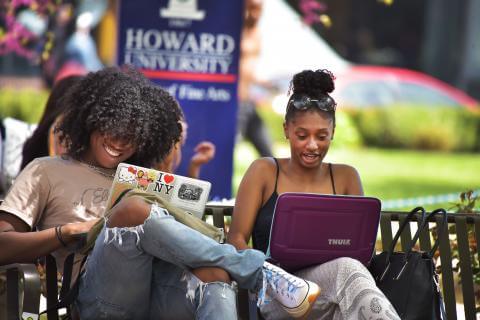 Howard University students using laptops outside.