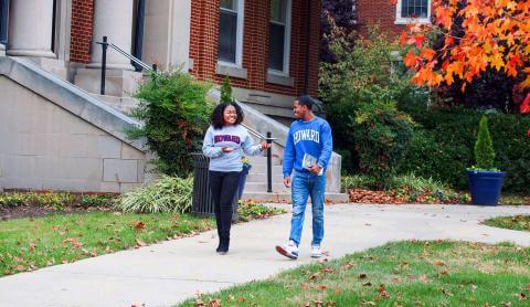 Two students in Howard University brand shirts walking on campus on an autumn day.